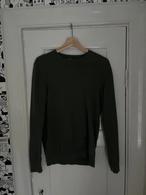Mörkgrön tröja från Dressmann S - En stilren mörkgrön tröja från Dressmann i storlek S. Tillverkad i mjuk Supima-bomull med rund hals och långa ärmar. Perfekt för dig som gillar en enkel och clean look. Passar till både jeans och chinos.