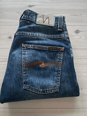 Nudie Jeans Grim Tim - Snygga Grim Tim jeans från Nudie Jeans i shaded blue med klassisk orange söm på bakfickan. Bästa Nudie modellen med knapp jylff och en regulator/slim fit. Byxorna är in bra och använt skick. Hör av dig vid minsta intresse 