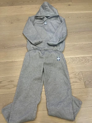 Brazil tracksuit - Säljer en enkel grå hoodie med huva och långärmad design. På bröstet finns ett blått och vitt emblem. Tröjan är gjord i mjukt bomullsmaterial och har en normal passform, perfekt för chill dagar eller träning. Matcha med dina favoritjeans eller mjukisbyxor. Pris kan ändras