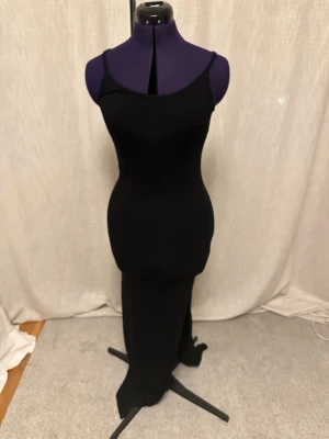 Svart långklänning med smala axelband skims doupe - En stilren svart långklänning med smala justerbara axelband och figurnära passform. Klänningen har en enkel och elegant design utan mönster eller detaljer, perfekt för dig som gillar minimalistisk stil. Materialet känns mjukt och stretchigt. Jag har även klippt slits och sytt ett stopp. 