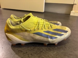 Adidas Crazyfast gula fotbollsskor - Säljer ett par Adidas Crazyfast fotbollsskor i en fräsch gul färg med svarta och blå ränder på sidan. Skorna har snörning, platt sula med orange dobbar och en lätt, syntetisk ovandel som ger bra känsla på planen. Perfekt för dig som vill ha speed och stil på matchen. Köpta för 2700kr.
