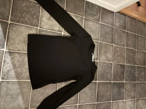 Svart långärmad tröja från 157 - En stilren svart långärmad tröja från 157, perfekt för dig som gillar enkla och klassiska plagg. Tröjan har rund hals och är gjord i mjuk bomull som känns skön mot huden. Passar dig som vill ha en basic topp till garderoben. Den är lite sönder under armen men sydde igen de men den öppnat sig lite men de syns inte på 