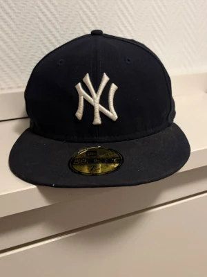 Svart New Era 59FIFTY NY-keps - Säljer en klassisk svart New Era 59FIFTY keps med New York Yankees-logga framtill i vitt broderi. Kepsen har rak skärm och MLB-logga bak. Tillverkad i 100% polyester och har en snygg, stilren look.
