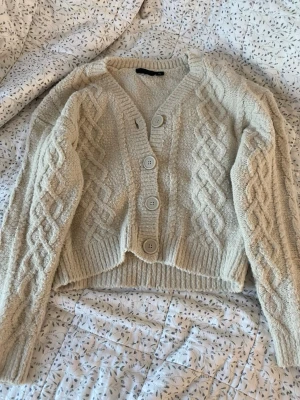 Beige stickad kofta med flätmönster - Mysig beige stickad kofta med stora knappar och snyggt flätmönster på både ärmar och framstycke. 
