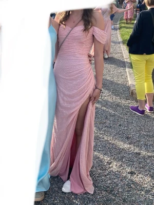 Rosa glittrig långklänning med slits - Säljer en fin rosa långklänning med glittrigt tyg och offshoulder-ärmar. Klänningen är lång men tajt så en xs för långa, till en ca 165-170 cm lång tjej. Den är använd 1 gång under en kväll så den är i bra skick. Den kommer med i en hängande klädpåse. 🩷