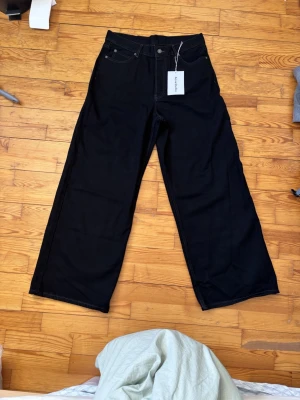 Svarta wide jeans från Acne Studios - Säljer ett par svarta jeans från Acne Studios med breda ben och klassisk femficksdesign. Jeansen har vita kontrastsömmar, hög midja och är tillverkade i kraftig bomull. Perfekta för dig som gillar en loose och trendig siluett.