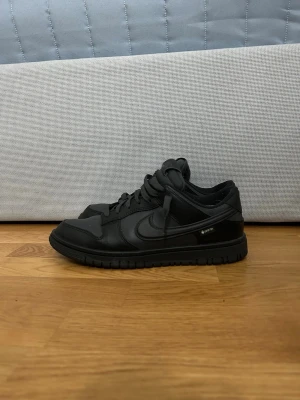 Nike Dunk Low Gore-Tex Svart EUR 41 - Ordinarie pris 1600kr! Nike Dunk Low Gore-Tex i helsvart färg med snygg robust design. Skorna har en platt sula, rund tå och är tillverkade i skinn och syntetmaterial. De har snörning och Gore-Tex-detalj på sidan för extra väderskydd. Perfekt för dig som gillar streetwear och vill ha något som tål regn.