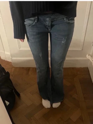 Blå bootcut jeans med låg midja - Säljer ett par snygga blå bootcut low waist jeans i bra skick. Väldigt unika och fina med en slit över benet som ni ser på bilden! Passar bra till både sneakers och klackar!