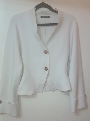 Vit cardigan jacka från Gina Tricot - Säljer en stilren vit cardigan jacka från Gina Tricot. Jackan har en croppad passform, långa ärmar med breda muddar och två stora knappar framtill. Materialet känns mjukt och har en lätt struktur. Perfekt för dig som gillar minimalistisk och clean stil.