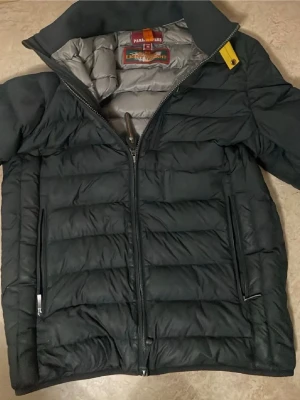 Svart dunjacka från Parajumpers S - Säljer en svart dunjacka från Parajumpers i storlek S. Jackan är quiltad med två dragkedjefickor framtill och har en snygg gul detalj vid kragen. Lättviktig och perfekt för kyliga dagar. Innerfodret är grått och jackan har hel dragkedja framtill.