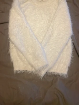 Vit fluffig tröja från SAMSA Young - Supermjuk och fluffig vit tröja från SAMSA Young i storlek 146/152. Tröjan har långärmade ärmar och ribbade muddar vid ärmslut och nederkant. Perfekt för dig som gillar mysiga och stilrena plagg med lite extra fluff.