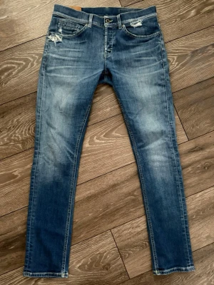 Blå skinny jeans från Dondup - Säljer ett par blå skinny jeans från Dondup med slitna detaljer vid fickorna och snygg tvätt. Jeansen har klassisk femficksdesign, normal midja och är tillverkade i mjukt denimtyg. Perfekta för dig som gillar en smal passform och vill ha ett par stilrena jeans.