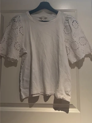 Vit blus med broderade puffärmar - Supersöt vit blus med puffärmar i broderad spets och rund halsringning. Ärmarna har fina hålmönster och vågig kant. Kroppen är i mjuk bomull och toppen har en avslappnad passform. Perfekt för dig som vill ha något romantiskt och trendigt.