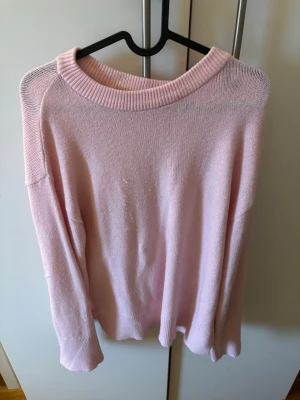 Ljusrosa stickad tröja med rund hals - Mysig ljusrosa stickad tröja med rundad hals och ribbade muddar vid ärmslut och nederkant. Tröjan har en loose passform och långa ärmar, perfekt för att chilla eller hänga med kompisar. Enkel och stilren design som är lätt att matcha med jeans eller kjol. Lite katt riv märken därav att jag har katter men annars i fint skick