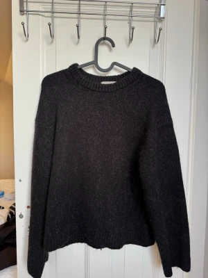 Svart stickad tröja från Gina Tricot - Mysig svart stickad tröja från Gina Tricot med rund halsringning och ribbade muddar. Perfekt för kyliga dagar och enkel att matcha med allt. Tröjan har använts en del och är ganska urtvättad (se bilder), därmed säljs den billigt. 