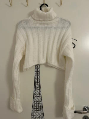 Vit stickad croppad polotröja från Chiquelle  - Croppad polotröja i vit stickad kvalitet från Chiquelle i storlek XS. Tröjan har långa ärmar med uppvikta muddar och ribbad struktur. 