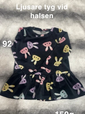 Svart klänning med kaninmönster - Supersöt svart klänning med färgglada kaniner i rosa, gult och lila. Klänningen har lång ärm och volang nedtill, perfekt för dig som gillar gulliga prints. Mjuk och skön, Rund hals med ljusare tyg på insidan.🌸 Mer sliten vid halsen och därav ser man vitare i botten. Storlek 92