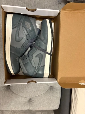 Nike Air Jordan 1 High grå sneakers - Säljer ett par Nike Air Jordan 1 High i olika nyanser av grått med vit sula och svarta detaljer. Skorna har klassisk snörning, rund tå och är tillverkade i en mix av skinn och mocka. Perfekta för dig som gillar streetwear och vill ha en ikonisk sneaker i garderoben. Riktig bekväm pris kan även diskuteras vid snabb affär.