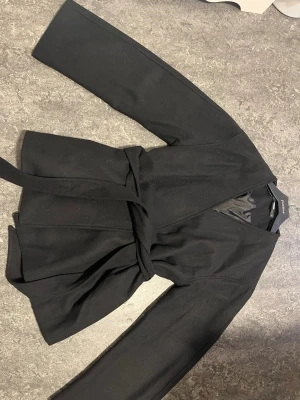 En svart Bikbok kappa - Säljer en svart kappa från Bikbok. Använd bara ett bara få gånger nästa helt ny storlek S.