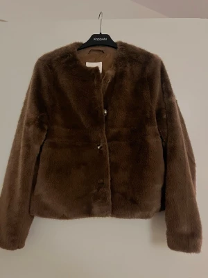 Brun pälsjacka från H&M - Mysig brun pälsjacka från H&M i storlek M. Jackan har en fluffig och mjuk känsla, stängs med knappar framtill och har långa ärmar. Perfekt för dig som vill ha en varm och stylish look under kyliga dagar.