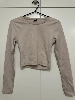 Träningstopp med cut-out – Gina Tricot - Beige croppad träningstopp med lång ärm från Gina Tricot. Stretchigt och bekvämt material, perfekt för gym, yoga eller promenader. Snygg cut-out i ryggen.