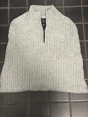  Stilren Grå Half-zip från JFK | Storlek S - Kan gå ner i pris ordentligt vid snabb affär! Tröjan har en snygg ribbad struktur som ger lite extra karaktär och en praktisk dragkedja i halsen. Den är perfekt att bära både till vardags över en t-shirt eller lite mer klätt över en skjorta. Skick: Jättegott skick! Inga fläckar, hål eller tecken på noppor. Sparsamt använd och väl omhändertagen. Passform: Normal i storleken med bra stretch tack vare ribbstickningen. 