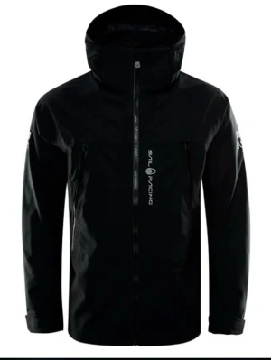 Svart vindjacka från Sail Racing - Svart vindjacka från Sail Racing med huva och hel dragkedja framtill. Jackan har stilren design med logga på bröstet och praktiska fickor med dragkedja. Perfekt för blåsiga dagar och outdoor-aktiviteter.