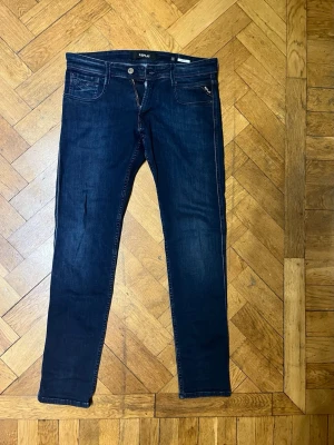 Mörkblå Replay Anbass jeans - Säljer ett par mörkblå Replay Anbass jeans med klassisk femficksdesign och smal passform. Jeansen har snygga kontrastsömmar och diskret Replay-logga på fickan. Perfekta för dig som gillar stilrena och tidlösa jeans med modern look.