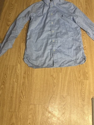 Blå skjorta från Polo Ralph Lauren - Säljer min feta ljusblå skjorta från Polo Ralph Lauren i slim fit-modell. Skjortan har lång ärm, knappar framtill och ikoniska broderade loggan på bröstet. Tillverkad i mjuk bomull och passar perfekt till en clean och stilren look. Ingen stor defekt utom att skjortan har en lite fläck som jag tyvärr inte vet om det går att ta bort men, annars är det inget problem med skjortan passar storlek small, och ett bra skick på skjortan, meddela gärna mig om ni har någon fråga!😁