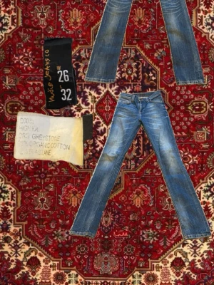 Nudie Jeans blå jeans W26 L32 - Säljer ett par klassiska blå jeans från Nudie Jeans i modellen High Kai. Jeansen har slim passform, snygga slitningar och kontrastsömmar. Tillverkade i ekologisk bomull med stretch för extra komfort. Fickor både fram och bak samt ikonisk Nudie-brodyr på bakfickorna. Lägg gärna prisförslag 