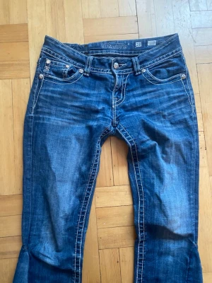 Blå Miss Me jeans med broderi - Säljer ett par blå Miss Me jeans med snygga broderade detaljer och nitar på bakfickorna. De är köpta på Plick men tyvärr för stora för mig. Jeansen har sytts ut där nere sedan innan. Låg midja och bootcut-ben. 