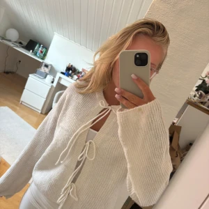 Vit stickad kofta med knytband - Superfin vit stickad kofta med tre knytband framtill. Koftan har långärmade, lite vidare ärmar och ribbad struktur. Perfekt att slänga över ett linne för en chill och mysig look.