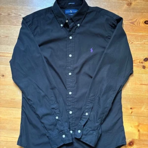 Polo Ralph Lauren Skjorta - Säljer min Ralph Lauren-skjorta – Slim Fit, strl M 🙌🏼🔥 Superfin svart skjorta från Ralph Lauren med lila brodyr, Slim fit som sitter riktigt snyggt 👌🏼  ✅ Storlek: M 👕 ✅ Slim fit – stilren & bekväm 🙌🏼 ✅ Mycket bra skick – sparsamt använd 🌟  Perfekt både till vardag & fest