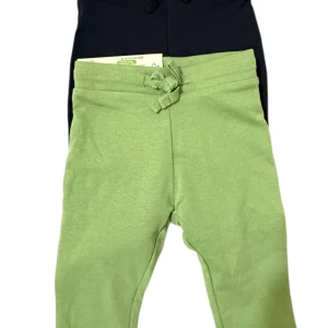 2-pack baby mjukisbyxor svart & grön - Två par mjukisbyxor i svart och ljusgrön färg, båda med snörning i midjan. Byxorna har en enkel, rak passform och är tillverkade i mjukt bomullsmaterial. 