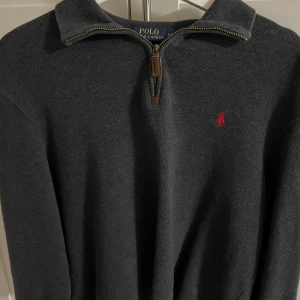 Mörkgrå stickad tröja Polo Ralph Lauren - Str S-M Mörkgrå stickad tröja från Polo Ralph Lauren med halv dragkedja och klassisk röd broderad logga på bröstet. perfekt för lager-på-lager perfekt till hösten