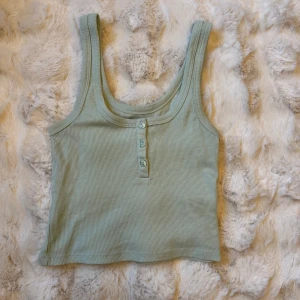 Mintgrön ribbad linnetopp 157 S - Superfin mintgrön ribbad linnetopp från 157 med tre knappar framtill. Toppen är ärmlös och har en croppad passform som passar perfekt till höga jeans eller shorts. Mjuk och stretchig bomullskvalitet som känns skön mot huden.