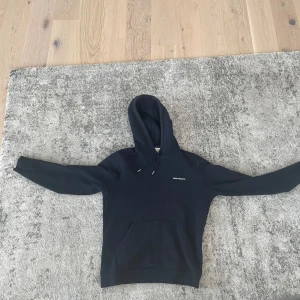 Marinblå hoodie från Norse Projects S - Svart hoodie från Norse Projects i storlek S. Klassisk modell med huva och dragsko, samt magficka framtill. Tillverkad i mjuk bomull och har en liten vit logga på bröstet. Perfekt för en chill och stilren look. Nypris ca 2000kr mitt pris 300kr