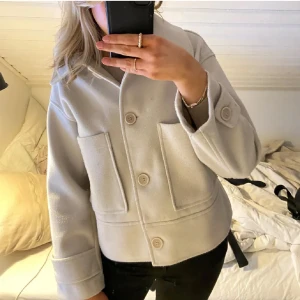 Beige ulljacka från Kappahl - Snygg beige jacka från Kappahl i ullmix med stora fickor framtill och klassisk krage. Jackan är croppad med raka ärmar och stängs med stora knappar. Perfekt för dig som gillar stilren och trendig look. Ganska nopprig men går säkert att få bort, annars bra skick! Nypris 899