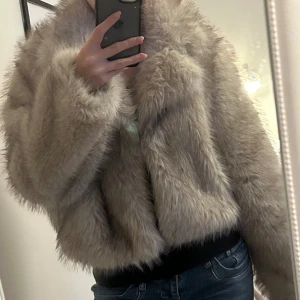 Beige fluffig pälsjacka - Säljer en supermjuk och fluffig beige pälsjacka med bred krage och lång ärm. Jackan har en loose passform och är perfekt för dig som vill ha en cozy och trendig look. Materialet är syntetpäls som känns lyxigt och värmande. Passar dig som gillar statement-plagg.