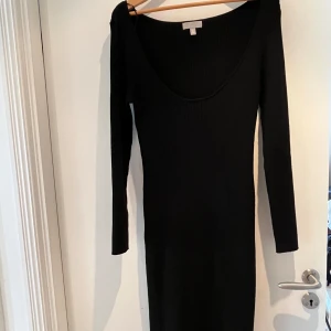 Svart ribbad långärmad klänning H&M - Svart ribbad långärmad klänning från H&M med djup urringning fram. Klänningen är figurnära och har en enkel, stilren design som passar perfekt till sneakers eller boots. Materialet är stretchigt och bekvämt, vilket gör den lätt att bära hela dagen.