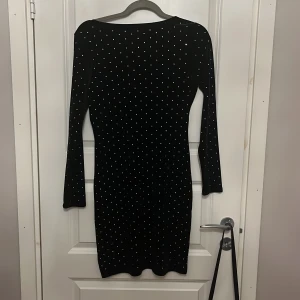 Svart glittrig sammetsklänning H&M M - Supersnygg svart sammetsklänning från H&M i storlek M. Klänningen har långa ärmar, tight passform och är täckt av små glittriga silverprickar. Djup urringning i ryggen och kort längd gör den extra trendig. Materialet är mjuk sammet med återvunnen polyester.