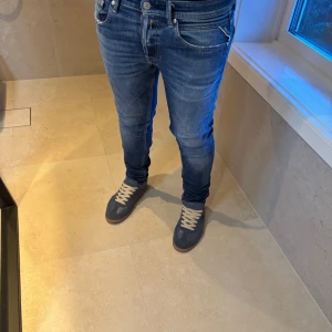 Replay Jeans. - Säljer ett par blå slim fit jeans med klassiska fem fickor och snygga sömdetaljer på bakfickorna. Jeansen har låg midja och är tillverkade i stretchigt denim för en tight passform. Perfekta för dig som gillar en modern och slimmad look.