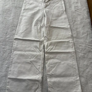 Vita raka jeans med hög midja - Snygga vita jeans med raka ben och hög midja. Klassisk femficksmodell med dragkedja och knapp framtill. Perfekta till sneakers eller boots för en clean look. Materialet är stadigt och passar året runt.