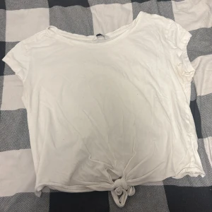 Vit knyt-topp i ekologisk bomull - Vit kortärmad topp från Cubus i ekologisk bomull. Modellen har en enkel och clean look med rund halsringning och en snygg knutdetalj framtill. Perfekt för en chill och avslappnad stil.