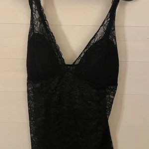 Svart spetstopp  från Lindex M - Supersnygg svart kort klänning från Lindex i genombruten spets med blommigt mönster. Ärmlös modell med smala axelband och v-ringning. Perfekt för dig som vill sticka ut med en elegant och trendig look.