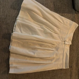 Vit plisserad kjol från FB Sister - Supersnygg vit plisserad kortkjol från FB Sister. Kjolen har klassiska veck och stängs med dragkedja och knapp i sidan. Perfekt för en trendig och fräsch look, lätt att matcha med olika toppar och sneakers.