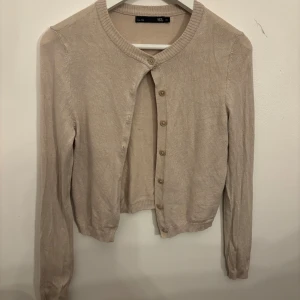 Beige rosa kofta från 157 XS - Beige rosa kofta från 157 i storlek XS. Klassisk rund halsringning, ribbade muddar och knäppning framtill med matchande knappar. Perfekt att slänga över en topp eller klänning för en chill look.