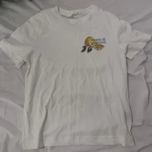 Vit t-shirt med citrontryck från H&M - Vit t-shirt från H&M i bomull med coolt citrontryck och texten 'aroma di limoni' på bröstet. Klassisk passform och rund halsringning, perfekt för en fräsch och somrig look. HELT NY