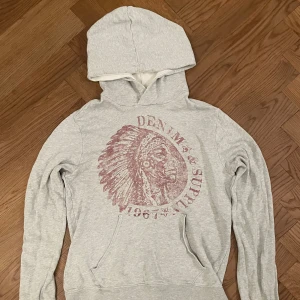 Grå hoodie från Denim & Supply - Ljusgrå hoodie från Denim & Supply med stor röd vintageinspirerad print framtill. Tröjan har huva, magficka och långa ärmar. Perfekt för allt! 