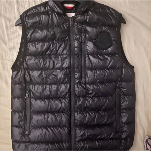Svart Moncler Väst - Svart Moncler Väst i storlek 1/S. Använd fåtal gånger men har tyvär ett litet hål som syns på bild 4. Annars är den som ny. Mitt pris 800kr